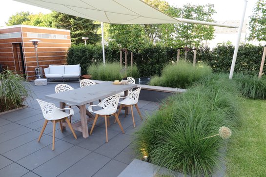 Terrasse mit modernen Gartenmöbeln, Sonnensegel, Umpflanzung mit Gräsern und Zierlauch, Sonnensegel und Gartenhaus