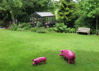 Wiese mit Gewächshaus und pinkfarbenen Schweinen aus Kunststoff