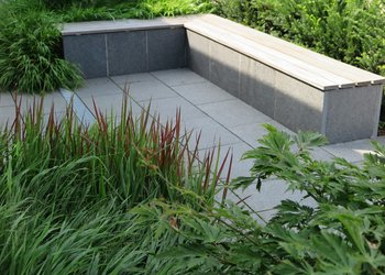 Garten für Ästheten mit rechteckiger Sitzbank mit Holzauflage und Umpflanzung mit Gräsern und japanischem Blutgras