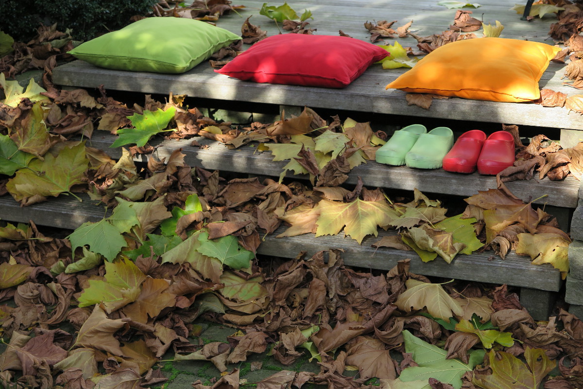 Holzterrrasse und Treppe mit bunten Kissen und buntem Herbstlaub bedeckt