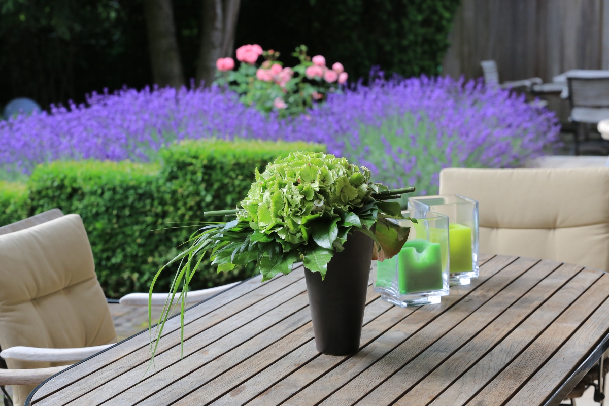 ein Gartentisch aus Holz vor einem Beet aus Lavendel mit rosa Rosen