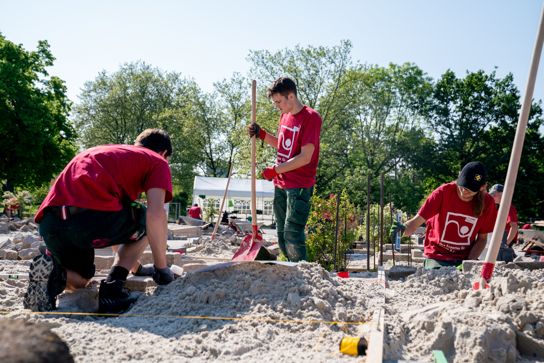 Gartenbau-Team bei Erdarbeiten, Sandfläche und Pflanzbereich im Freien Verschiedene Beerensträucher, darunter Sanddorn, Hagebutte, Eberesche und Liguster, in unterschiedlichen Farben.
